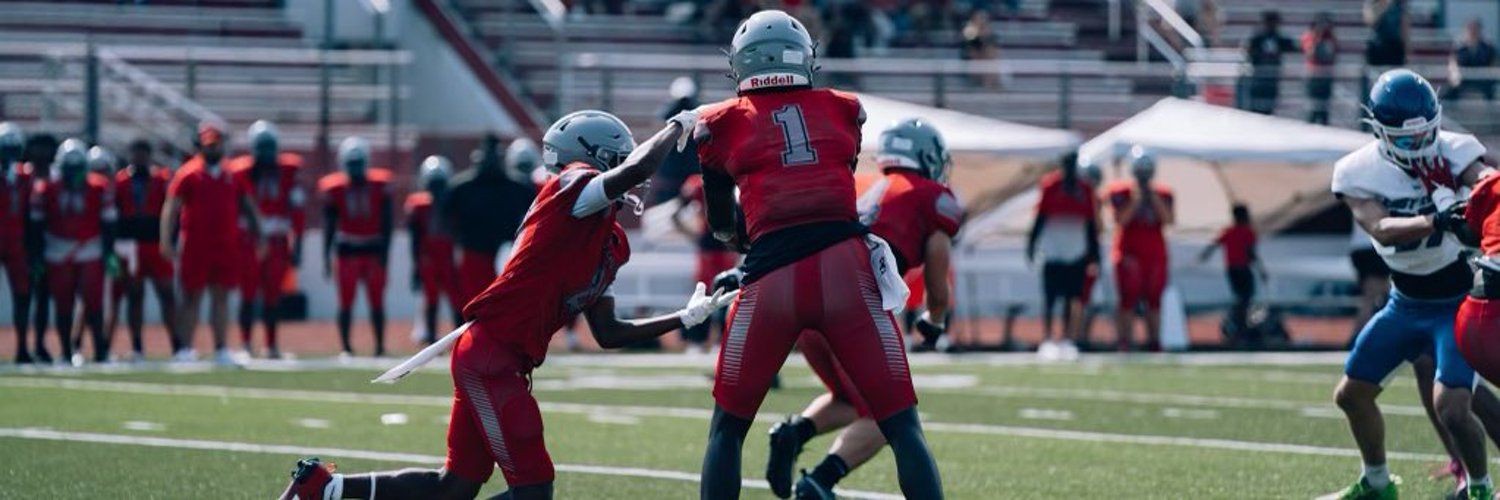 High school football game with players in red and blue jerseys on a green field during a match.