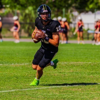 Football player in black uniform runs with the ball on a grass field during a game.